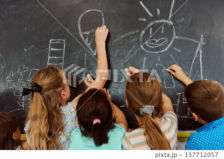 Children drawing together on a chalkboard in a playful elementary classroom activity 137712057