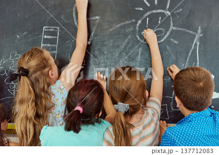 Children drawing together on a classroom chalkboard, teamwork and creativity in elementary school Children drawing together on a classroom chalkboard, teamwork and creativity in elementary school 137712083
