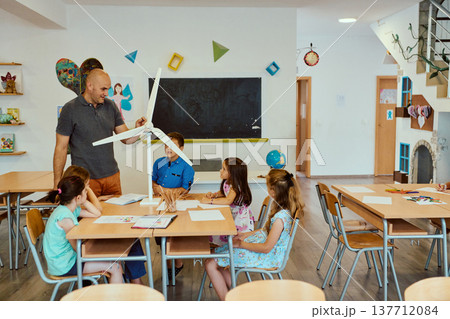 Teacher showing wind turbine model to elementary students in a bright classroom group lesson 137712084