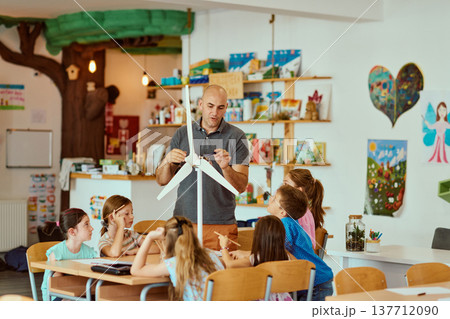 Teacher demonstrating a wind turbine model to engaged elementary students in a colorful classroom science lesson 137712090