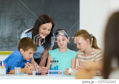 Teacher guiding elementary students through a hands-on science experiment in classroom Teacher guiding elementary students through a hands-on science experiment in classroom 137712141