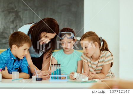 Teacher guiding children through a hands-on science experiment with test tubes in a classroom 137712147