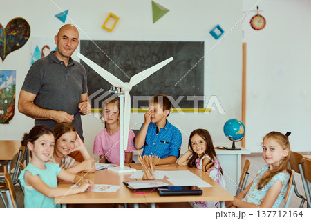 Teacher leading elementary students building a model wind turbine during a classroom STEM lesson 137712164