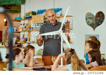 Teacher demonstrating a model wind turbine to children in a hands-on STEM classroom lesson on renewable energy 137712169