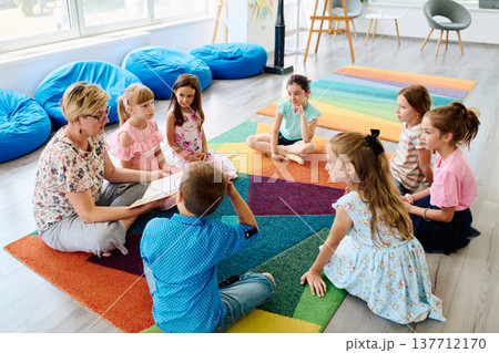 Teacher reading a story to children during circle time in a colorful preschool classroom 137712170