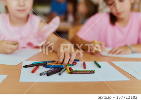 Children reaching for colorful crayons while drawing together at a classroom table 137712182