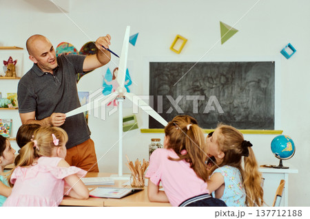 Teacher demonstrating model wind turbine to elementary students during hands-on STEM lesson in classroom 137712188