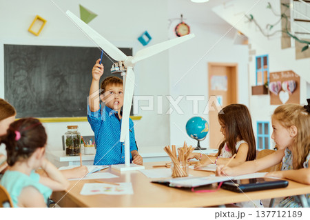 Children in a classroom exploring a wind turbine model during a hands-on STEM science lesson 137712189