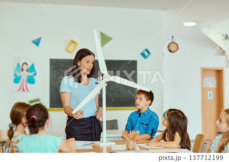 Teacher leads elementary classroom lesson on renewable energy using a wind turbine model with curious students engaged in hands-on science learning 137712199
