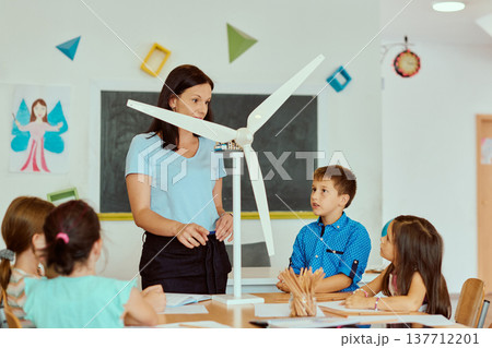 Teacher explaining wind turbine model to elementary students in classroom during renewable energy lesson Teacher explaining wind turbine model to elementary students in classroom during renewable energy lesson 137712201