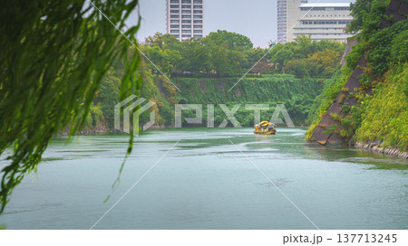 Osaka, Japan - Sep 22 2024, panoramic view of the moat around Osaka Castle on which a yellow tourist boat floats, view from the bridge through foliage and a tree branch, on a rainy day, Osaka, Japan 137713245