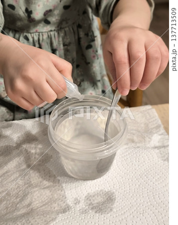 A girl mixes a solution in a plastic cup with a spoon. A girl mixes a solution in a plastic cup with a spoon. 137713509