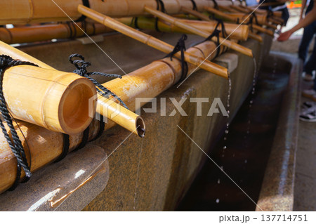 Kyoto, Japan - Sep 23 2024, close-up view Tsukubai stone bathtub with bamboo pipes through which water flows, at background people wash their hands, at entrance to Fushimi Inari shrine, Kyoto, Japan Kyoto, Japan - Sep 23 2024, close-up view Tsukubai stone bathtub with bamboo pipes through which water flows, at background people wash their hands, at entrance to Fushimi Inari shrine, Kyoto, Japan 137714751