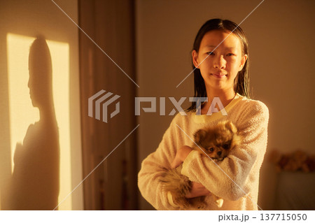 家の寝室で朝の日差しを浴びて子犬を抱っこする可愛い女子中学生の姿	 137715050