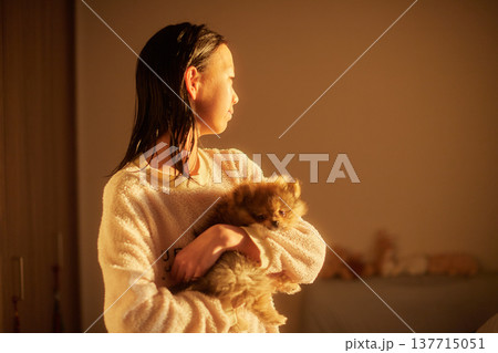 家の寝室で朝の日差しを浴びて子犬を抱っこする可愛い女子中学生の姿	 137715051