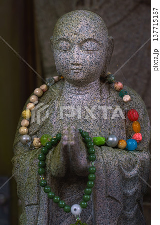 Kyoto, Japan - Sep 23 2024, A close-up view of a stone statue of man with beads on its neck and rosary of colorful beads on its hands, an altar on the territory of Fushimi Inari Temple, Kyoto, Japan Kyoto, Japan - Sep 23 2024, A close-up view of a stone statue of man with beads on its neck and rosary of colorful beads on its hands, an altar on the territory of Fushimi Inari Temple, Kyoto, Japan 137715187