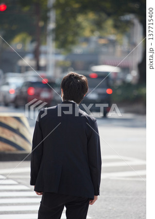 冬の昼の名古屋の繁華街の交差点で信号待ちの若い男性サラリーマンの姿	 137715400