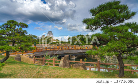 Himeji, Japan - Sep 24 2024, panoramic view of Sakuramon Bridge and entrance gate, with Himeji Castle, White Heron Castle on background, trees on foreground, at daytime with cloudy sky, Himeji, Japan 137716080