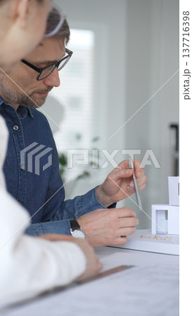 Architects collaborating on architectural plans. Designing modern building models. Drawing blueprints. Engineering innovative residential project solutions Architects collaborating on architectural plans. Designing modern building models. Drawing blueprints. Engineering innovative residential project solutions 137716398
