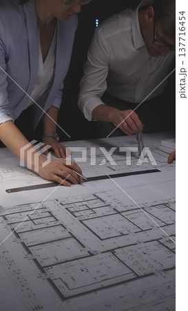 Architects collaborating on a modern house design, working with a scale model and engineering blueprints on a desktop. Concept of architecture and business in low key lighting Architects collaborating on a modern house design, working with a scale model and engineering blueprints on a desktop. Concept of architecture and business in low key lighting 137716454