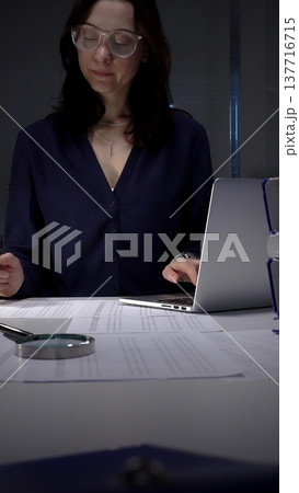 Woman working late night in office, multitasking with a tablet and writing on documents, managing heavy paperwork load. Audit and taxes in business Woman working late night in office, multitasking with a tablet and writing on documents, managing heavy paperwork load. Audit and taxes in business 137716715