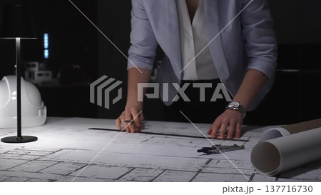 Architect hand drawing building plan, focused on engineering blueprints at office desk, hard hat nearby, late working hours 137716730