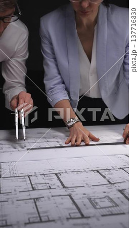 Architects and engineers collaborating on a building blueprint, measuring and discussing plans for a new construction project. Concept of architecture and business in low key lighting 137716830