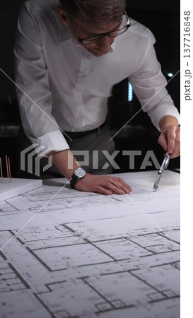 Architect working on blueprints using a compass, designing building plans in a studio at night. Concept of architecture and business in low key lighting 137716848