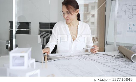 Professional female architect working on building plans in a modern office, drawing blueprints with a ruler and pen, designing new projects with focus and precision for urban development 137716849