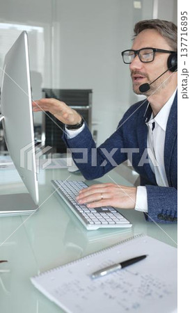 Man in headset talking during online video call, working in office, consulting remote customers, providing technical support. Business people concept Man in headset talking during online video call, working in office, consulting remote customers, providing technical support. Business people concept 137716895