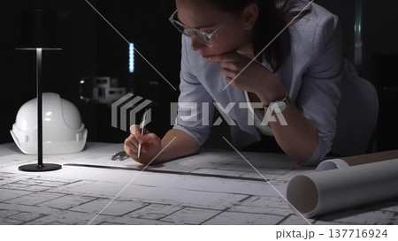 Female architect working late at night, drafting blueprints and engineering plans in a dark office. Business and architect people concept Female architect working late at night, drafting blueprints and engineering plans in a dark office. Business and architect people concept 137716924