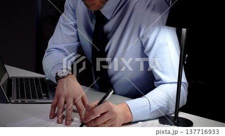 Professional businessman typing on laptop, working late in an office, demonstrating dedication and diligence. Audit and taxes in business 137716933