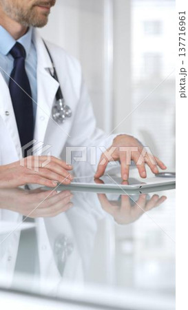 Doctor using tablet computer, providing healthcare consultation, digital medical technology, professional man in lab coat. Medicine and health care Doctor using tablet computer, providing healthcare consultation, digital medical technology, professional man in lab coat. Medicine and health care 137716961