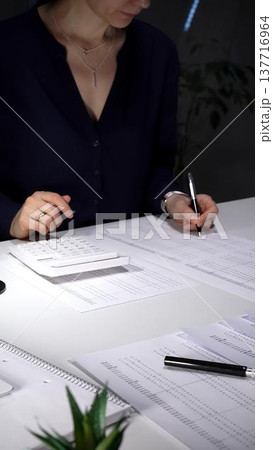 Woman working late night, calculating expense reports, reviewing financial documents with focused attention. Audit and taxes in business Woman working late night, calculating expense reports, reviewing financial documents with focused attention. Audit and taxes in business 137716964
