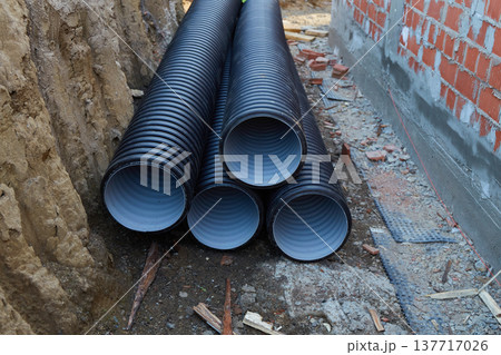 Workers are concentrated at a construction site where several black pipes are stacked on the ground. Workers are concentrated at a construction site where several black pipes are stacked on the ground. 137717026