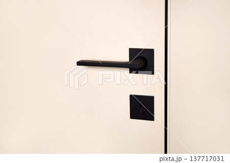 A black door handle is mounted on a smooth white wall. Modern door with hidden installation A black door handle is mounted on a smooth white wall. Modern door with hidden installation 137717031