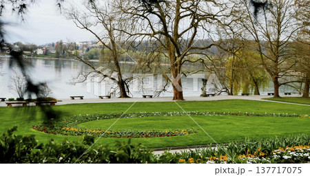 Garden near the river with trees and colorful flowers during a cloudy day in springtime Garden near the river with trees and colorful flowers during a cloudy day in springtime 137717075