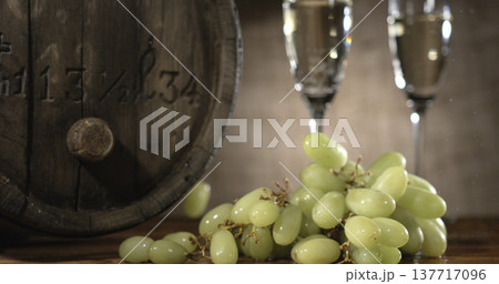 Grapes and champagne glasses are placed beside a wooden barrel in a warm setting during a festive gathering 137717096