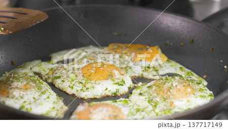 Cooking eggs in a frying pan with herbs in a kitchen during the morning hours 137717149