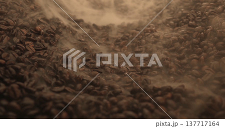 Freshly roasted coffee beans in a dark roasting chamber with smoke rising above them Freshly roasted coffee beans in a dark roasting chamber with smoke rising above them 137717164