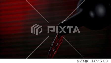 Red liquid pours from a bottle against a dark background with hints of red light in a simple setting Red liquid pours from a bottle against a dark background with hints of red light in a simple setting 137717184