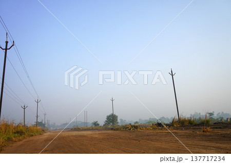 Wide Perspective of a Dusty Rural Road with Utility Poles Under a Clear Blue Morning Sky 137717234