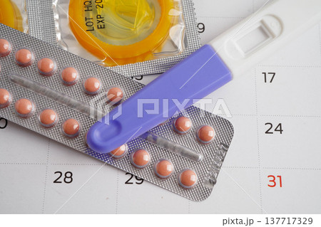 Pregnancy test with birth control pills and condom for female on calendar, ovulation day. Pregnancy test with birth control pills and condom for female on calendar, ovulation day. 137717329