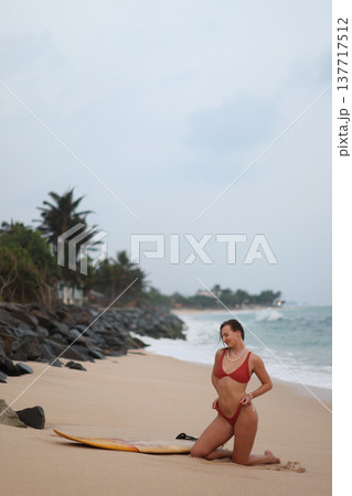 Tranquil Seaside Setting Showing Woman In Bikini Preparing For Surf Amidst Palm Trees And Sandy Beach 137717512