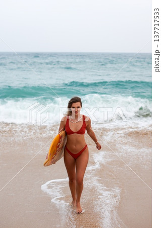 Beach Girl Smile. Lively Female Surfer In Red Bikini Navigating Incoming Waves With Joyful Enthusiasm 137717533