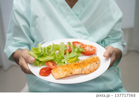 Asian elderly woman patient eating salmon stake and vegetable salad for healthy food in hospital. 137717568