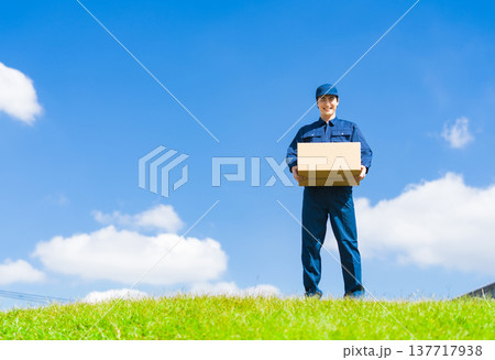 青空の下で荷物を持つ配達員・デリバリースタッフの男性 青空の下で荷物を持つ配達員・デリバリースタッフの男性 137717938