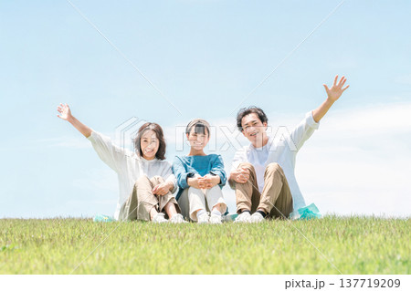 青空の見える公園・丘に座る家族・親子（父親・母親・娘） 137719209