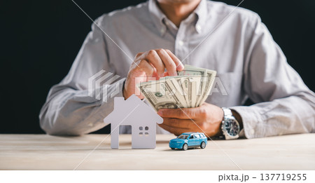Man holds dollar bills, representing home, car, property, house insurance loan for new real estate business concept, investment strategy for personal wealth planning shown with models 137719255