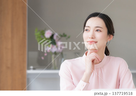 デスクで座るパソコンの仕事をするピンクの服を着た綺麗な女性　考える悩むポーズ 137719518
